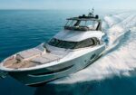 Luxury white motor yacht cruising at speed on calm blue sea, leaving a foamy wake behind it.
