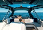 Open-air yacht deck with white cushioned seating, a wooden table, and a blue ocean view.