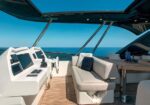 Modern yacht cockpit with steering wheel, multiple navigation screens, and beige seating against a blue ocean backdrop.