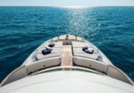 View from the bow of a luxury motorboat as it sails on a blue sea with sunlit water ahead.