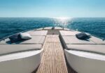 Twin sun loungers on the bow of a luxury yacht, facing the open sea with sunlight reflecting on the water.