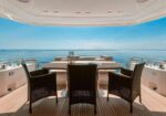 Outdoor dining table with four wicker chairs on a yacht deck overlooking the blue sea and horizon.