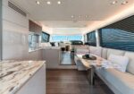 Luxurious yacht interior with marble dining table, white sofas, and large windows with blinds.