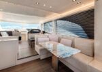 Luxurious yacht salon with cream seating around a marble dining table and large windows showing the ocean view.