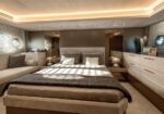 Luxurious modern bedroom with a large bed, built-in cabinets, and a plush sofa along the left wall in a warmly lit room with porthole windows and striped blinds.