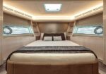 Luxurious yacht cabin with a large bed, neutral bedding, and soft overhead lighting in a beige-toned interior.
