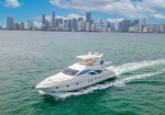 White luxury motor yacht cruising on turquoise water with a city skyline in the background