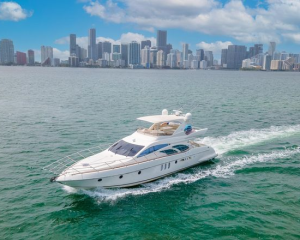 White luxury motor yacht cruising on turquoise water with a city skyline in the background
