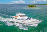 White luxury motor yacht cruising in turquoise water near a small island with a distant skyline on a sunny day
