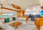 Luxurious yacht salon with cream leather seating, green cushions, and a round wooden coffee table beside large windows over the water.