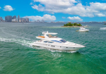 White luxury motor yacht cruising on turquoise water with a distant city skyline and a small island on the horizon.
