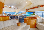 Luxurious yacht salon with cream leather seating, curved white ceiling, and wood cabinetry; TV shows a tropical island.