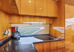 Wood-paneled boat galley with a coffee maker, electric stove, and a window showing water outside.