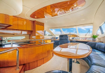 Luxurious yacht salon with glossy wood panels, curved seating around a polished table, and a helm in the background.