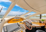Luxurious boat cockpit with a wooden dashboard, steering wheel, and navigation screens under a sunlit canopy.