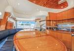 Luxurious yacht salon with a glossy wooden dining table, blue leather seating, and built-in cabinets with an ocean view through large windows.