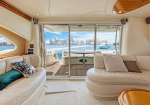 Luxurious cream‑themed yacht salon with curved seating and cushions, opening to a deck with water and a city skyline in the distance.