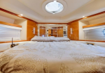 Luxurious boat cabin with a large bed, patterned duvet, round hatch above, and glossy wood cabinets along the sides.