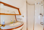 Small bathroom on a boat with an oval sink, wood trim, and a mirrored vanity; a compact enclosed shower to the right.