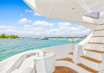 Luxurious white yacht deck with wooden steps, calm turquoise water, and other boats on a sunny day.
