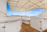 Yacht deck with white curved seating, wooden floor, and a beige canopy under a blue sky.