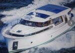 White motor yacht speeding through open water, wake behind it, viewed from above with a blue-roofed cabin area.