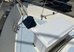 Cockpit of a sailboat with ropes and hardware, a blue canvas cover over gear, and a white hull near a parked truck in a marina.