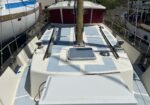 View from the deck of a boat showing a central mast, light blue hatch panels, and maroon canvas around the cabin; other boats and dock equipment sit on either side in a marina.