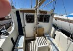 View down the cockpit of a small sailboat at a marina, with ropes hanging from the mast and steps leading up to the deck.