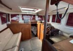 Cozy boat cabin with beige seating, wooden cabinets, and a steering wheel in the foreground; skylight overhead.