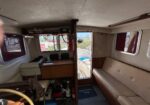 Cozy boat cabin with beige seating, wooden cabinet, and mounted nautical equipment; open deck visible through doorway to outside sea.