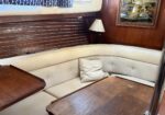 Wood-paneled boat cabin with a cream curved sofa, beige pillows, and a small lamp; a framed Levi Strauss & Co. sign on the wall.
