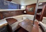Wood-paneled boat cabin with cream leather seating, a U-shaped dinette, and a window with patterned curtains.