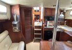 Interior of a wooden boat cabin with cream seating, stairs, and galley appliances along light-colored floor.