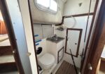 Compact boat head: toilet with sink, hoses, and nautical fixtures in a small, wood-trimmed bathroom.