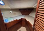 Cozy boat cabin with a wooden bunk bed, beige walls, and round porthole windows on either side.
