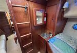 Wood-paneled cabin with a small mirror cabinet, red fire extinguisher, and built-in bunks along the wall; blue patterned bedspread visible in foreground