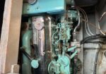 Teal-painted engine in a cramped compartment with exposed hoses, pipes and metal panels.
