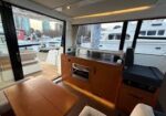 Interior of a yacht cabin with wooden cabinetry, seating, and a helm station, overlooking a marina outside the large windows.