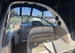 Inside a boat cabin with beige leather seating, a small white table, and large curved windows showing a marina outside.