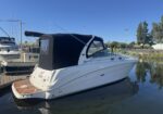 White motorboat with a black canvas cabin cover docked at a marina under a clear blue sky.