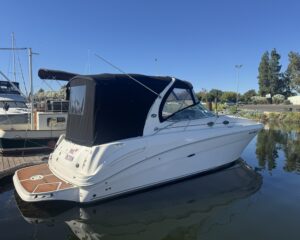 White motorboat with a black canvas cabin cover docked at a marina under a clear blue sky.