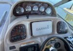 Boat cockpit dashboard with wooden panel and four analog gauges, Garmin unit, and steering wheel visible.