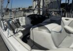 Interior of a white/gray motorboat with a steering console, cushioned seating, and blue accents; marina with boats in the background