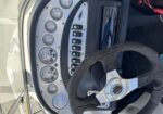 Boat helm dashboard with gauges, switches, and a textured steering wheel used to steer a boat.
