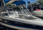 Powerboat with chrome wakeboard tower and blue canopy parked in marina.