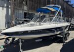 White speedboat on a trailer beside a weathered wooden fence and workshop items nearby.