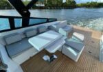 Luxurious yacht deck with white cushioned seating around a fold-out table on teak flooring, calm water in the background.