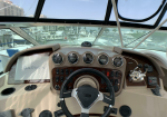 Boat cockpit helm with six gauges, steering wheel, Garmin display, and throttle levers, overlooking a marina.