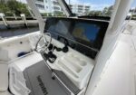 White boat cockpit with two large Garmin screens, steering wheel, throttles, and cup holders; marina view ahead.